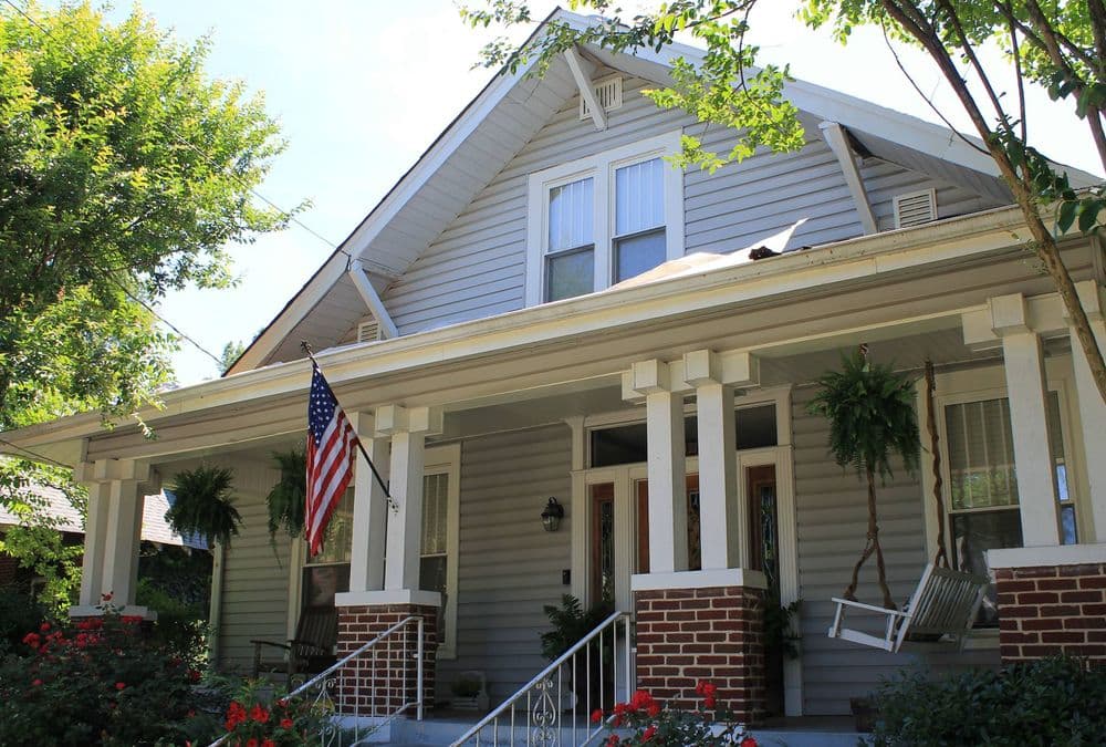 Two-story gray house with American flag, front porch, and landscaped garden.