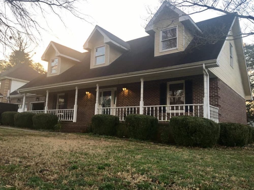 Charming two-story house with brick facade, porch, and neatly trimmed bushes in front yard.