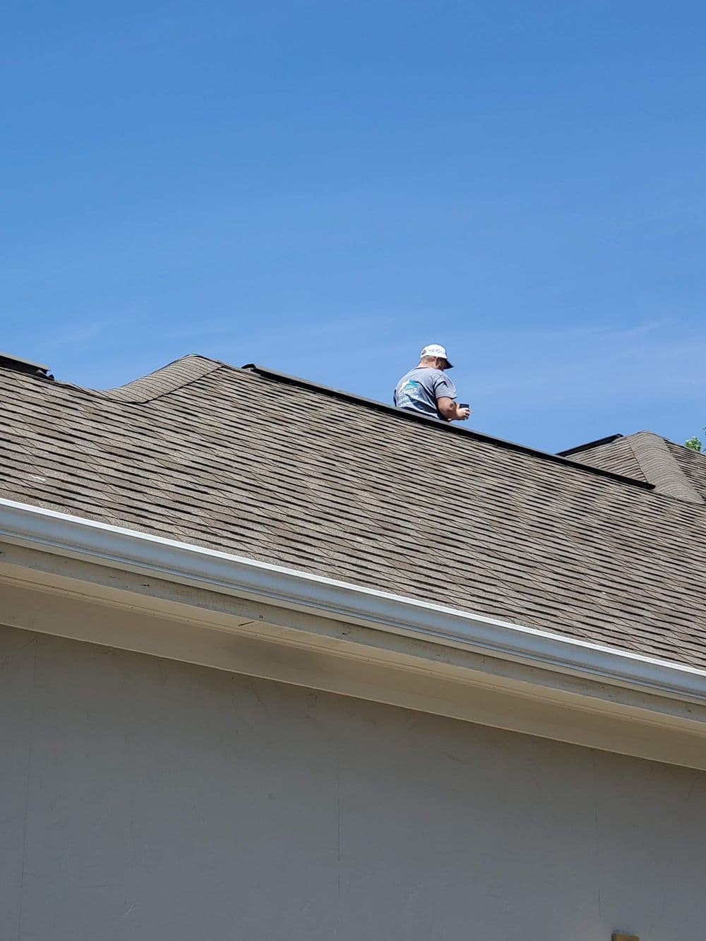 Roofer inspecting shingles on a house under a clear blue sky.