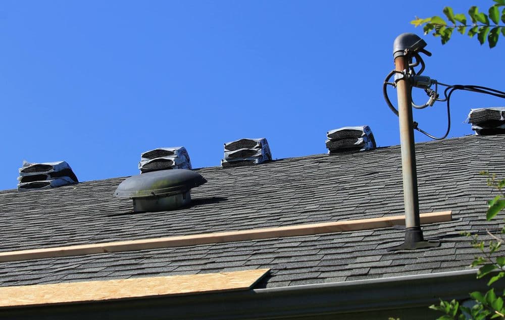 Roof with installed shingles, vent, and electrical pole against a clear blue sky.