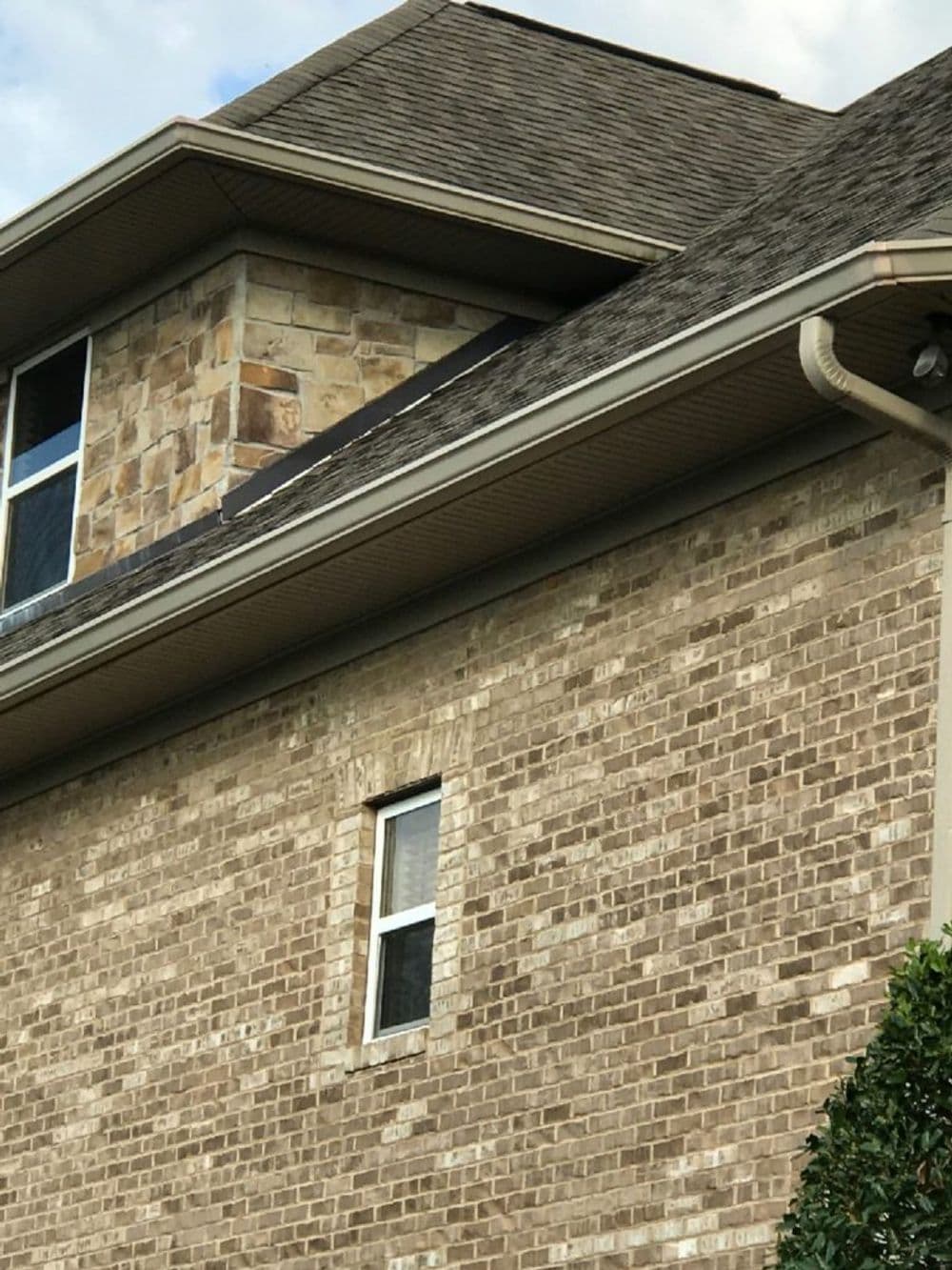 Brick house exterior with stone accents and a sloped roof under a partly cloudy sky.
