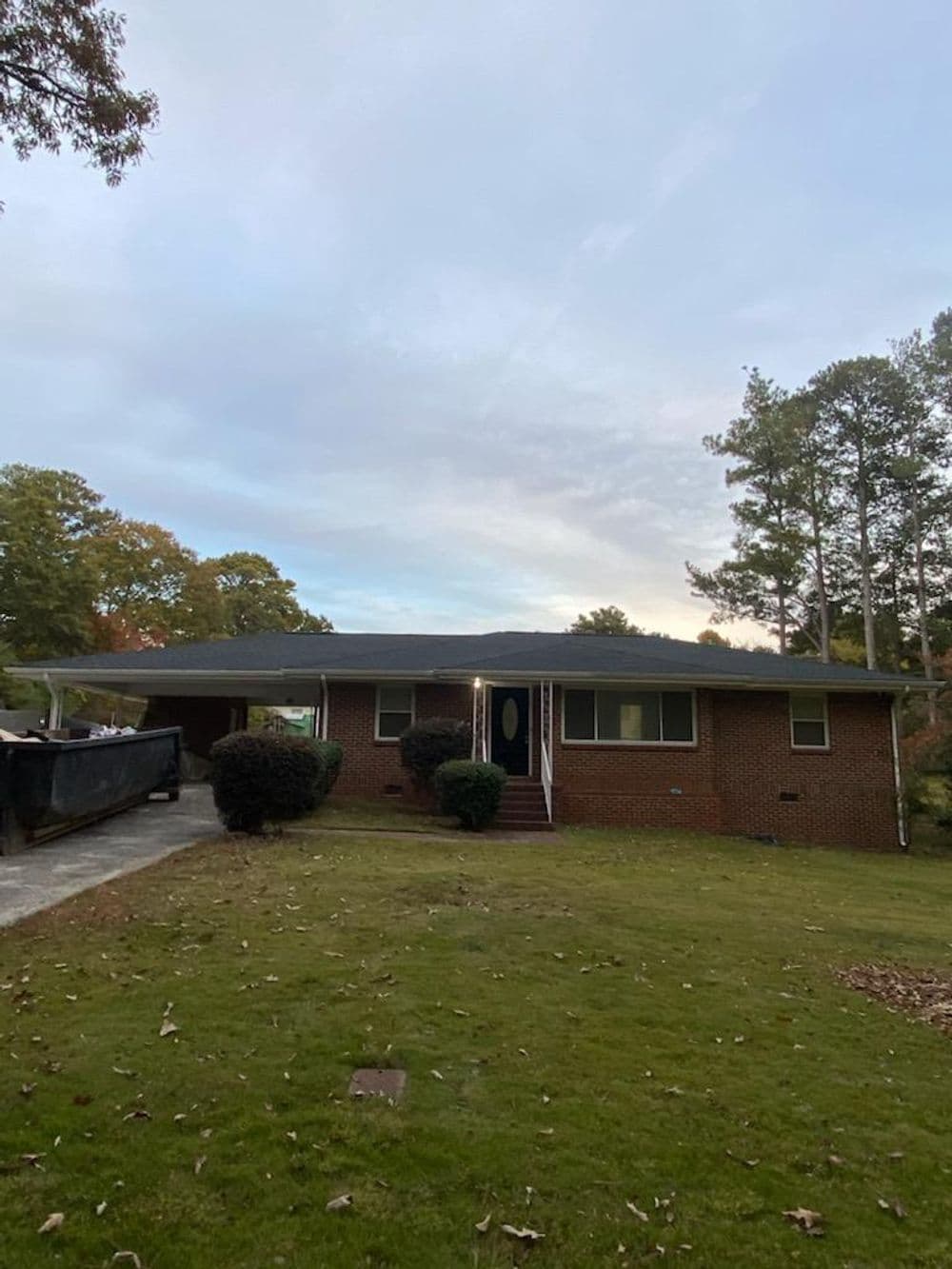 Brick house with a manicured lawn and trees, under a cloudy sky. Driveway to the left.