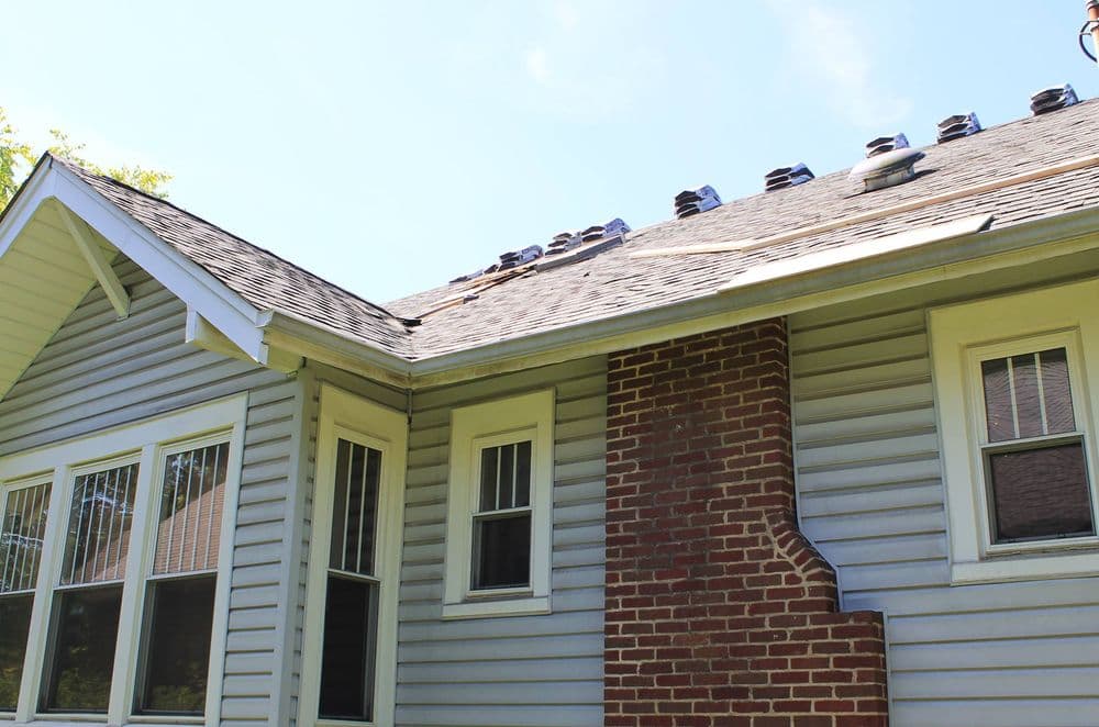 Residential home's roof showing shingles and brick chimney under a clear blue sky.