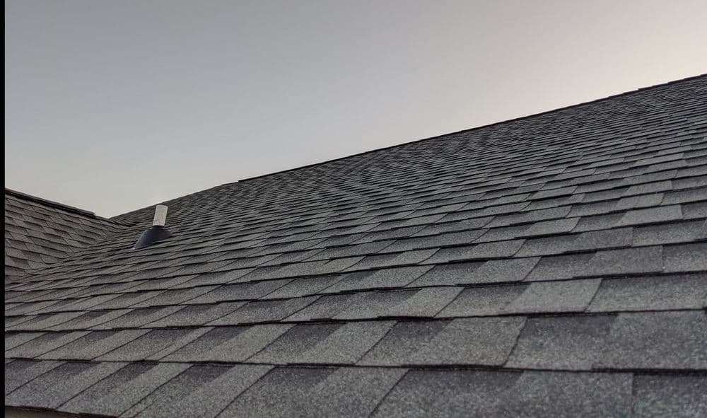 Roof with gray shingles and vent under a clear sky.