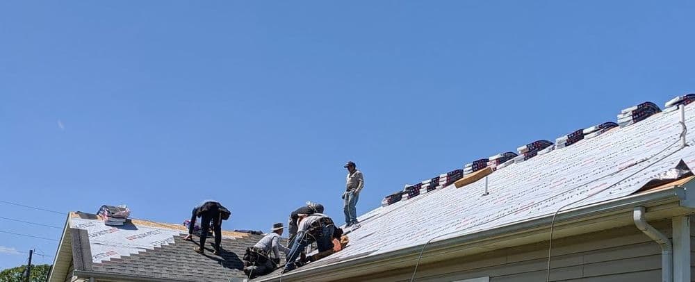 Roofing crew installing shingles on a home under clear blue sky.