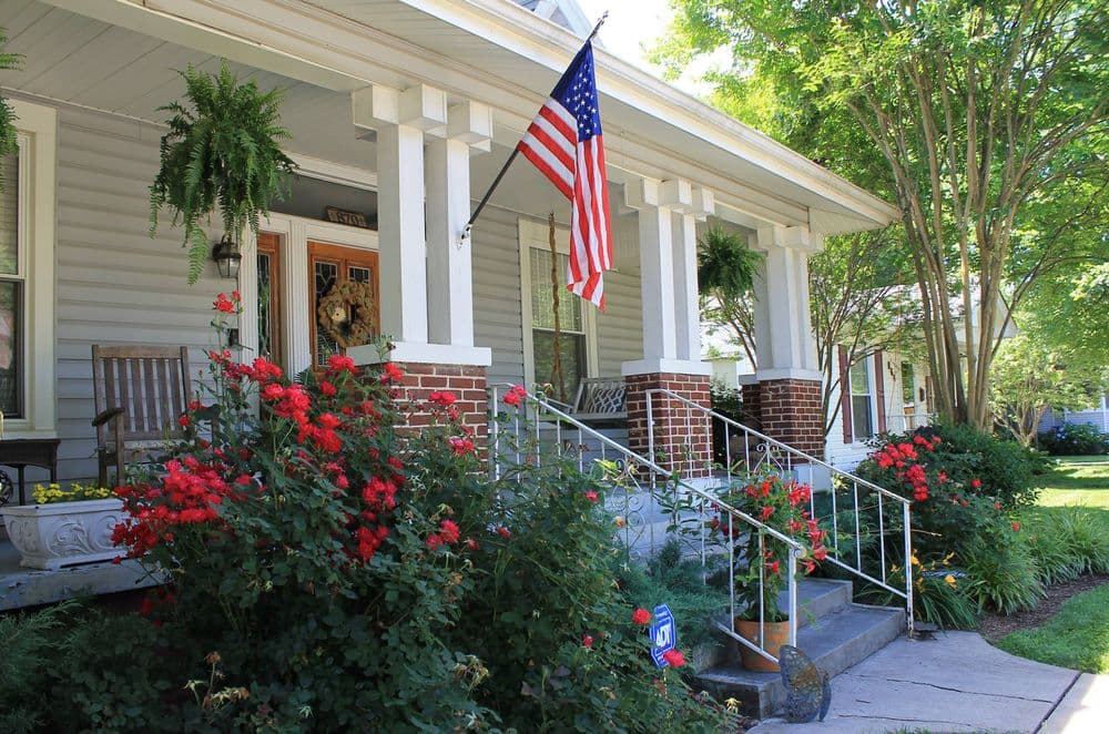 Charming porch with American flag and vibrant red flowers in bloom.