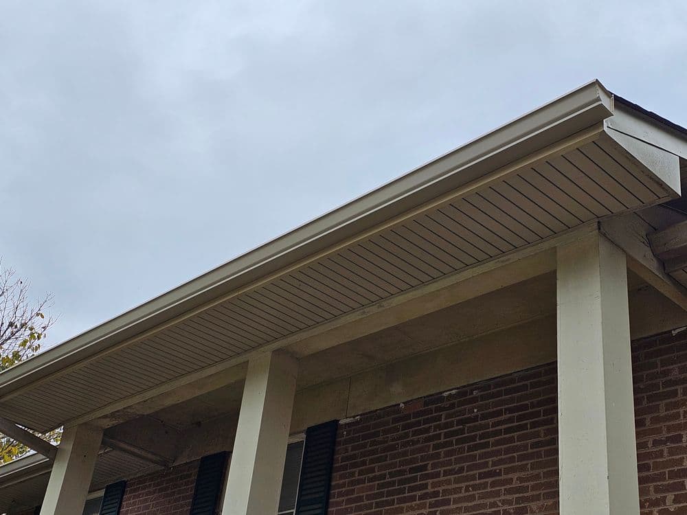 Underneath a residential eave with a cloudy sky in the background, showcasing detailed soffit design.