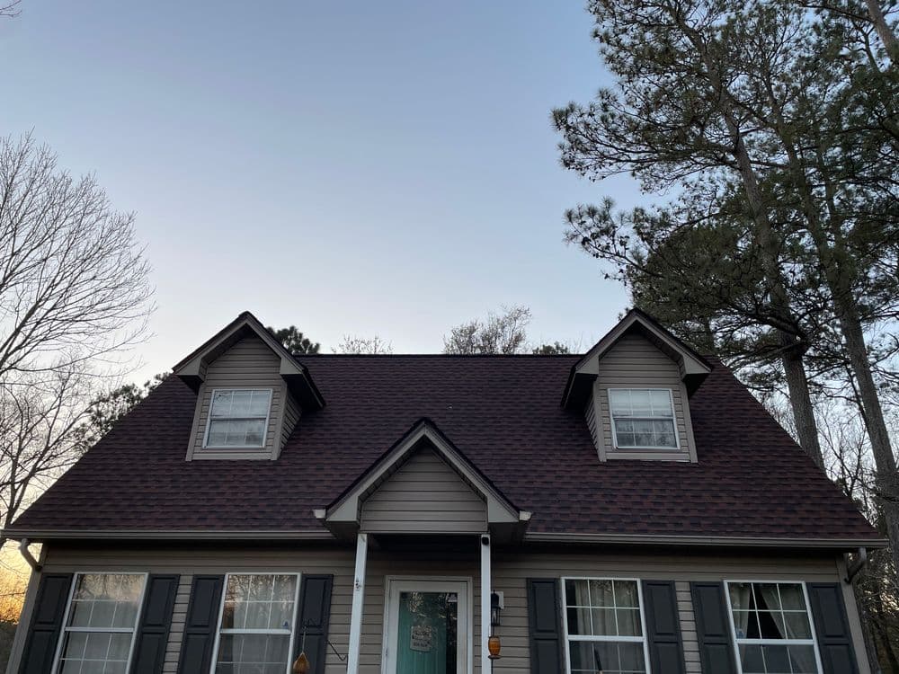 A cozy house with a peaked roof, surrounded by tall trees under a clear sky.