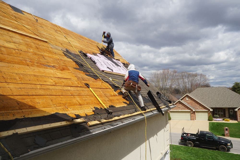 Workers installing a new roof on a house under a cloudy sky.